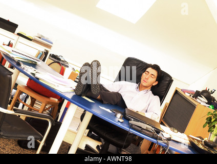 Mann, sitzend mit den Füßen auf Schreibtisch, Augen geschlossen Stockfoto