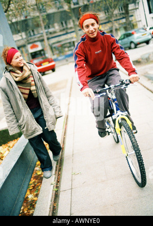 Zwei junge Menschen auf dem Bürgersteig, auf Fahrrad Stockfoto