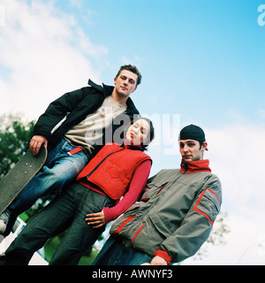 Drei junge Menschen, eine Holding-Skateboard, niedrigen Winkel Ansicht, Porträt Stockfoto