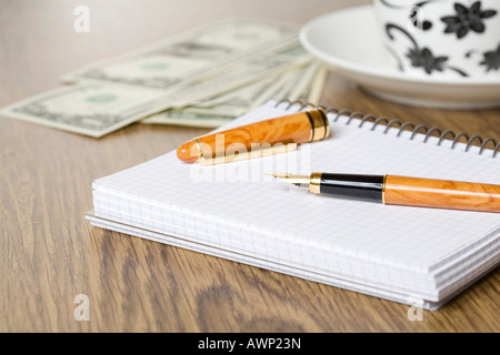 Füllfederhalter auf einem Tisch mit Notebook, US-Bargeld und Tasse und Untertasse Stockfoto