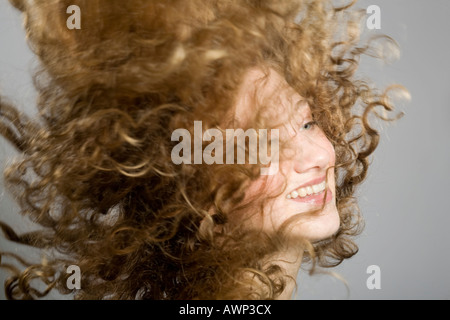 Junge Frau, ihr langes lockiges Haar durch die Luft fliegen Stockfoto