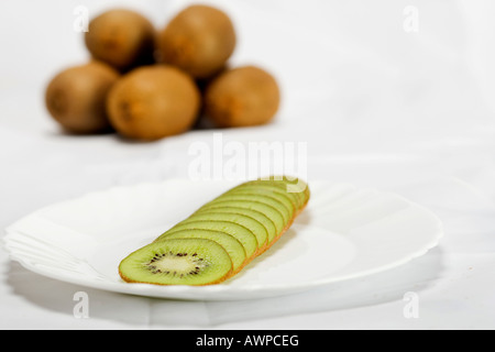 Einzelne geschnittene Kiwi auf einem Teller, mehr Kiwis gestapelt auf der Rückseite Stockfoto