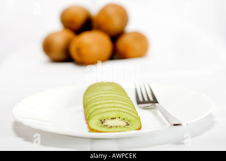 Einzelne geschnittene Kiwi auf einem Teller mit Gabel, mehr Kiwis gestapelt auf der Rückseite Stockfoto