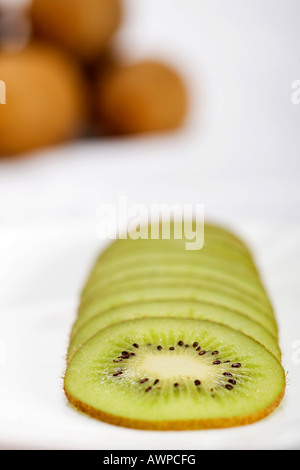 Kiwi Scheiben auf einen Teller mehr Kiwis gestapelt auf der Rückseite Stockfoto