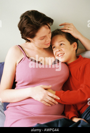 Schwangere Frau sitzend mit Arm um Kind Stockfoto