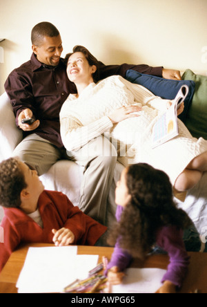 Mann und schwangere Frau auf Sofa, Kinder über Schulter bei Ihnen Stockfoto
