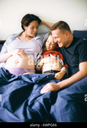 Paar und Kind zusammen im Bett, schwangere Frau und Kind zeigen Mägen Stockfoto
