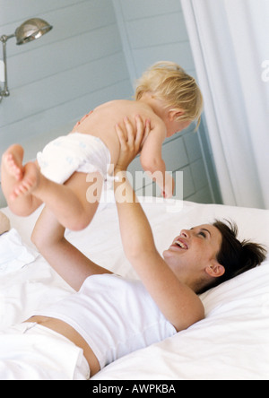 Frau auf Bett hält Baby in Luft Stockfoto