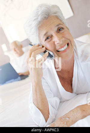 Ältere Frau mit Handy, Lächeln, Mann mit Laptop im Hintergrund Stockfoto