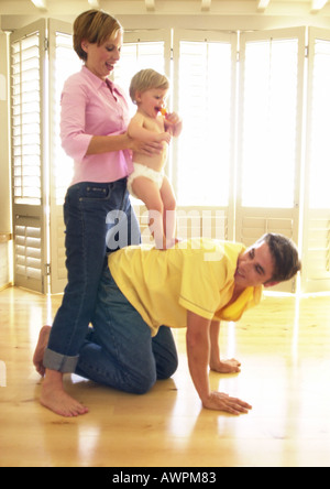 Mann auf allen Vieren, Frau halten Baby auf dem Rücken Stockfoto