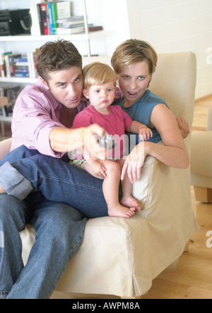 Paar halten Baby, auf Stuhl sitzend, zeigt Fernbedienung Stockfoto