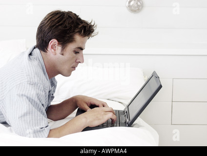 Mann liegt auf Bauch, mit Laptop-Computer, Seitenansicht Stockfoto