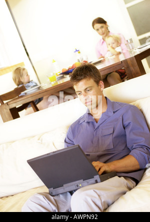 Frau und Kinder am Tisch, Mann mit Laptop auf sofa Stockfoto