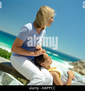 Mädchen mit dem Kopf auf Mutters Schoß, Meer im Hintergrund Stockfoto