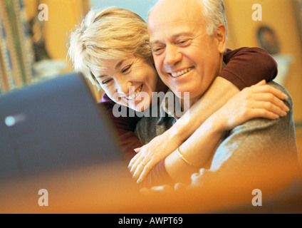 Älteres Paar, Lächeln, Mann mit Laptop, Frau mit Mann umarmt Stockfoto