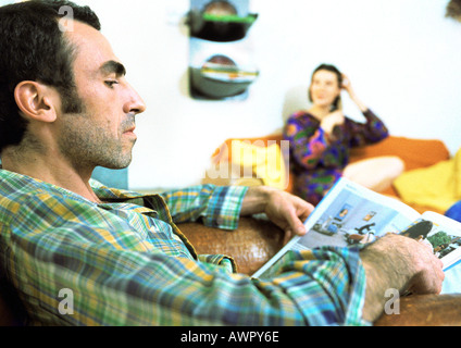 Mann liest Magazin, Frau im Hintergrund. Stockfoto