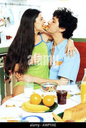 Paar am Frühstückstisch sitzen, enden Frau auf des Mannes Schoß, Essen aus der gleichen croissant Stockfoto
