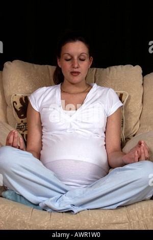 Junge hochschwangere Frau sitzt auf Sessel in Yoga Meditation position Stockfoto