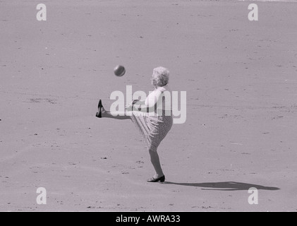 Ältere Frau, die Fußball spielen auf Strand-Wales Stockfoto