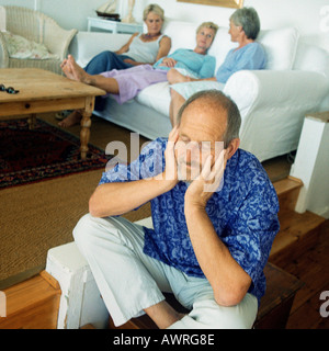 Reifer Mann sitzen auf Boden, drei Frauen im Hintergrund auf couch Stockfoto