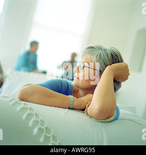 Reife Frau auf Sofa sitzen, Leute sitzen im Hintergrund Stockfoto