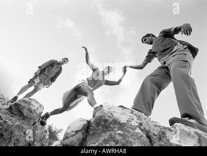 Drei Jugendliche klettern auf Felsen, Frau geholfen werden, niedrige Winkel Ansicht, b&w. Stockfoto