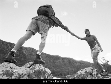 Mann hilft Frau über Felsen, niedrigen Winkel Ansicht, b&w. Stockfoto