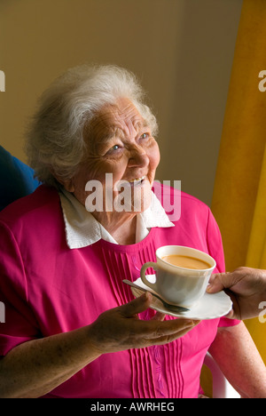 Pflege Die Pflege älterer Menschen glücklich TEESTUBE INSIDEHappy senior Alte ältere Dame erhält eine Tasse Kaffee von der Pflegeperson Begleiter Stockfoto
