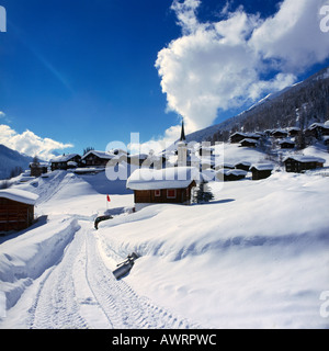 Reifenspuren im schweren Winter entlang einer Straße mit Chalets und Kirche jenseits in Biel Dorf das Goms-Tal der Schweiz Stockfoto