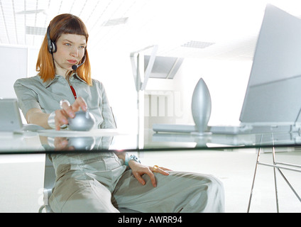 Frau trägt Kopfhörer, am Schreibtisch, drei Viertel Länge Stockfoto