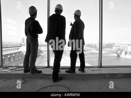 Drei Männer tragen Schutzhelme, Blick aus Fenster, Rückansicht, b&w Stockfoto