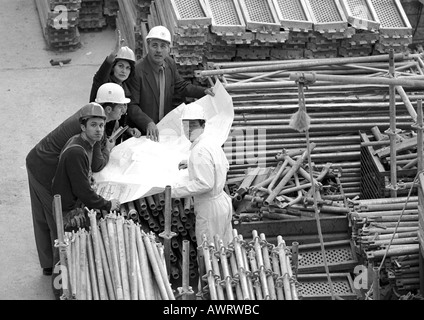 Fünf Personen untersuchen Blaupausen in Baustelle, Porträt, b&w Stockfoto