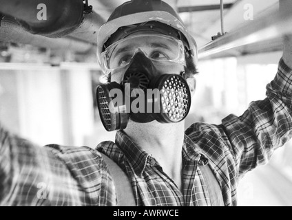 Mann mit Schutzhelm, Staubmaske und Schutzbrille, Nahaufnahme, b&w Stockfoto