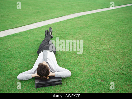 Mann liegt auf dem Rasen, Kopf auf Aktenkoffer Stockfoto