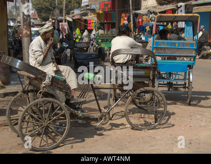 Rikscha oder Rikscha Fahrer warten auf Passagiere auf einer belebten Straße in der Mitte des Marktes von Agra, Indien. Stockfoto