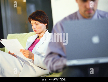 Geschäftsfrau Blick auf Dokument in der Nähe von Geschäftsmann auf Computer, unscharf Stockfoto