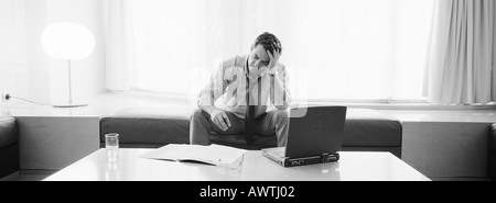 Geschäftsmann, sitzen halten Kopf, Laptop, Getränke und Dokumente auf Tisch vor ihm, b&w Blick Stockfoto