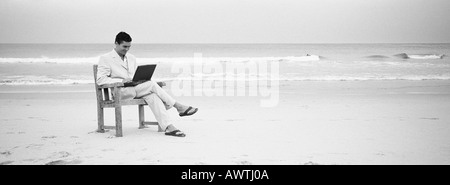 Mann sitzt im Stuhl am Strand mit Laptop, b&w, Panoramablick Stockfoto