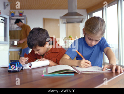 Sohn und Tochter schreiben an Tisch, Vater in der Küche Hintergrund unscharf. Stockfoto