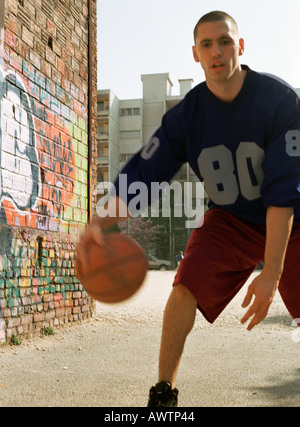 Mann dribbling Basketball in städtischen Spielplatz neben Graffitied Wand Stockfoto