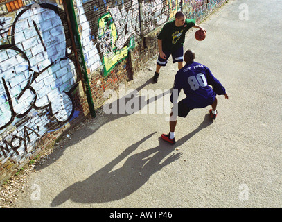 Zwei Männer spielen Basketball vor Graffitied Wand in städtischen Spielplatz Stockfoto
