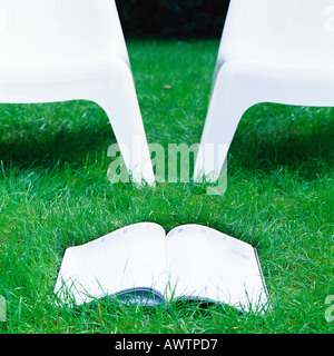 Offenes Buch in der Nähe von zwei Plastikstühle auf dem Rasen. Stockfoto