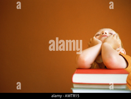 Kleiner Junge stützte sich auf Bücherstapel, Kopf in Händen Stockfoto