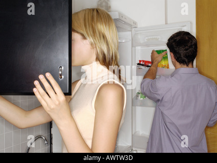 Junges Paar in der Küche, Frau Eröffnung Schrank Mann Element aus dem Kühlschrank nehmen Stockfoto