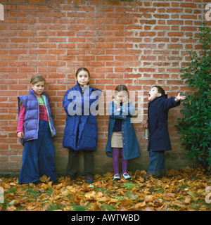 Vier Kinder tragen Mäntel vor Mauer, in voller Länge Stockfoto