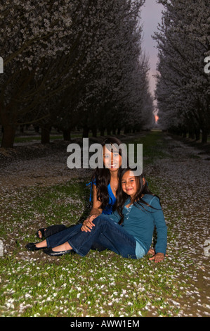 Mutter Tochter posiert sitzen am Boden Sonnenuntergang Mandel Obstgarten Stockfoto