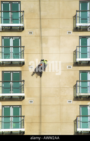 Arbeiter im Stuhl Gurt unterstützt vom Dach montiert Kabel Durchführung von Reinigungsarbeiten auf neue Wohnblocks Wand Stockfoto