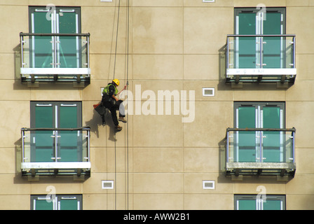 Arbeiter im Stuhl Gurt unterstützt vom Dach montiert Kabel Durchführung von Reinigungsarbeiten auf neue Wohnblocks Wand Stockfoto