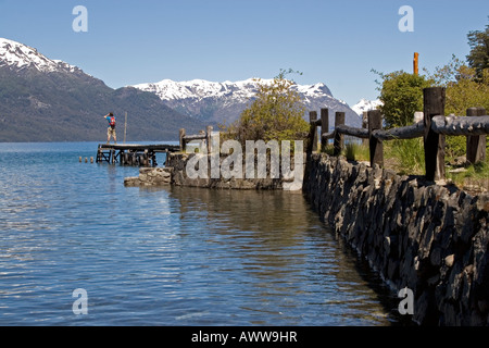 Fernen männlichen Figur Stand am Ende des See-Steg mit Fotografieren von schneebedeckten Bergen Stockfoto