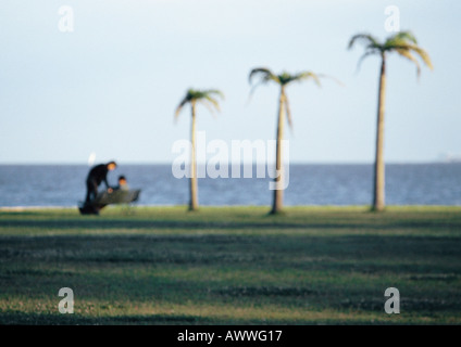 Zwei Menschen sitzen zusammen auf der Parkbank, Palmen drei vom Ozean, unscharf Stockfoto